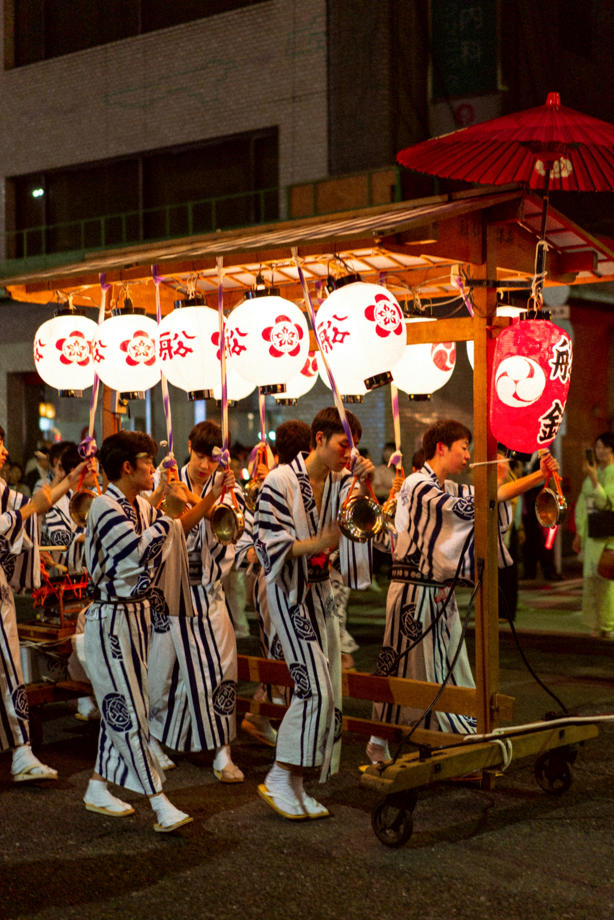 Young performers pull a traditional float through Kyoto’s streets during Gion Matsuri, lanterns glowing above them as bells ring out into the summer night.